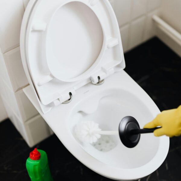 From above crop faceless person in yellow rubber cleaning gloves removing stains in toilet bowl with brush and detergent in washroom